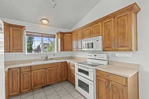 Kitchen featuring white appliances, lofted ceiling, brown cabinetry, light tile patterned flooring, and light countertops