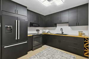 Kitchen with black appliances, light wood-style floors, dark cabinetry, and decorative backsplash