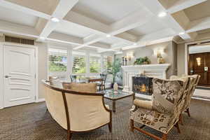 Lounge with dark colored carpet, beamed ceiling, coffered ceiling, a lit fireplace, and ornamental molding