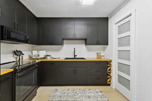 Kitchen featuring black appliances, butcher block counters, light wood-style flooring, dark cabinetry, and backsplash