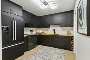Kitchen with black appliances, dark cabinets, light wood finished floors, butcher block countertops, and tasteful backsplash