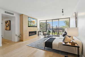 Living area featuring expansive windows, wood finished floors, a glass covered fireplace, rail lighting, and a view of city