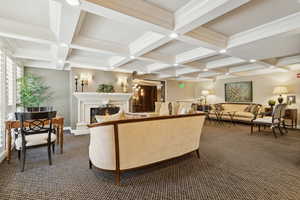 Lounge with dark colored carpet, beam ceiling, a warm lit fireplace, coffered ceiling, and ornamental molding