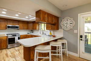 Kitchen featuring stainless steel appliances, a peninsula, brown cabinetry, light countertops, and a kitchen breakfast bar