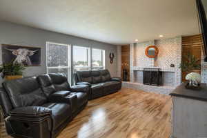 Living area with a brick fireplace, light wood-style floors, a textured ceiling, and recessed lighting
