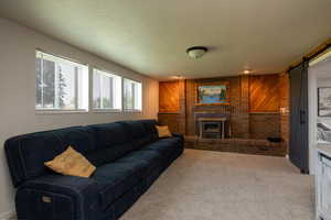 Living room featuring a barn door, carpet floors, a textured ceiling, and wood walls