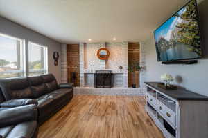Living area with a fireplace, light wood-type flooring, a textured ceiling, and recessed lighting