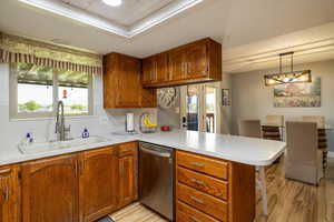 Kitchen with dishwasher, a peninsula, light wood-type flooring, and brown cabinets