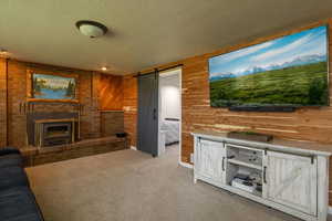 Unfurnished living room with a barn door, a textured ceiling, wooden walls, and carpet floors