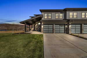 View of property featuring a garage, board and batten siding, concrete driveway, a front lawn, and stone siding