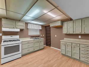 Kitchen featuring white gas range, under cabinet range hood, light wood-style flooring, a paneled ceiling, and light countertops