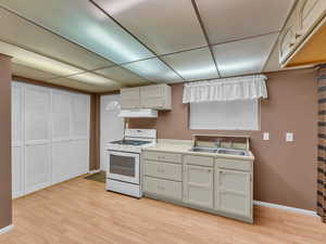 Kitchen featuring white gas range oven, under cabinet range hood, light wood-style floors, and light countertops