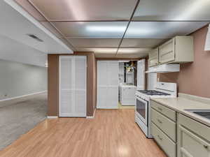 Kitchen featuring white gas stove, washer / dryer, under cabinet range hood, light countertops, and light wood-style flooring