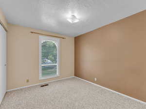 Carpeted empty room featuring a textured ceiling and baseboards