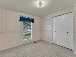 Unfurnished bedroom featuring wallpapered walls, a closet, carpet, and a textured ceiling