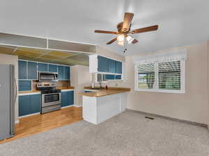 Kitchen with stainless steel appliances, blue cabinets, light carpet, a ceiling fan, and a peninsula