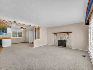 Unfurnished living room featuring a stone fireplace, a ceiling fan, carpet floors, and a textured ceiling