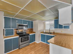 Kitchen featuring stainless steel appliances, blue cabinetry, light wood-style floors, a drop ceiling, and backsplash