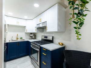 Kitchen with stainless steel gas range, blue cabinets, under cabinet range hood, white cabinetry, and recessed lighting