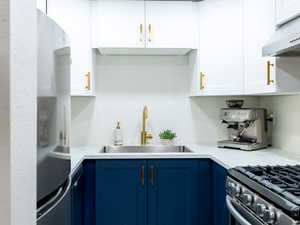 Kitchen with under cabinet range hood, blue cabinetry, freestanding refrigerator, and white cabinets