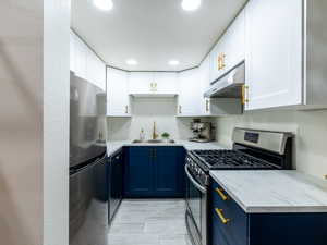 Kitchen with appliances with stainless steel finishes, blue cabinets, under cabinet range hood, white cabinets, and recessed lighting