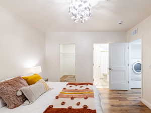 Bedroom featuring light wood-style flooring, a chandelier, washer / clothes dryer, a spacious closet, and ensuite bath