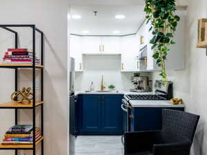 Kitchen featuring stainless steel gas range, blue cabinets, light countertops, white cabinetry, and under cabinet range hood