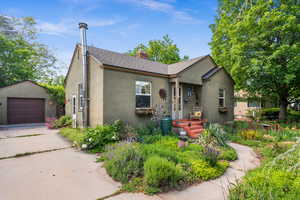 Bungalow with stucco siding, an outbuilding, a chimney, and concrete driveway