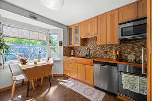 Kitchen featuring appliances with stainless steel finishes, backsplash, baseboards, a sink, and glass insert cabinets