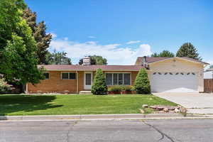 Ranch-style house with an attached garage, concrete driveway, brick siding, a front yard, and a chimney