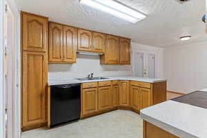 Kitchen featuring dishwasher, a textured ceiling, a peninsula, brown cabinets, and light countertops