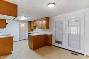 Kitchen with french doors, light countertops, brown cabinetry, a peninsula, and light flooring
