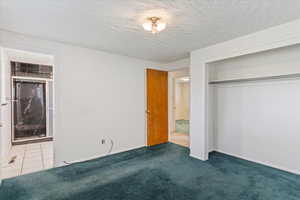 Unfurnished bedroom with carpet flooring, a closet, ensuite bath, and a textured ceiling