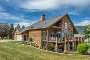 Rear view of house with stone siding, a chimney, a yard, driveway, and an attached garage