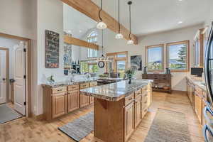 Kitchen featuring light wood-type flooring, hanging light fixtures, a kitchen island, high vaulted ceiling, and light stone counters