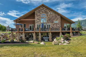 Back of property featuring a deck with mountain view, stone siding, and a yard