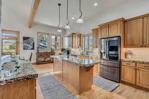 Kitchen with stainless steel refrigerator with ice dispenser, recessed lighting, tasteful backsplash, a kitchen island, and light stone counters