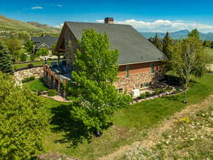 View of side of home with stone siding, a mountain view, a yard, and a shingled roof