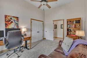 Office space with a ceiling fan, carpet, and a towering ceiling