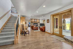 Living room featuring french doors, wood finished floors, stairway, recessed lighting, and a stone fireplace