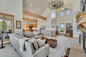 Living room with high vaulted ceiling, light carpet, a chandelier, and a glass covered fireplace
