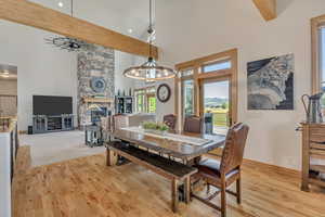 Dining area with a towering ceiling, light wood-type flooring, a chandelier, a stone fireplace, and recessed lighting