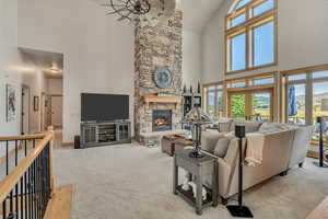 Carpeted living area with high vaulted ceiling, plenty of natural light, and a stone fireplace