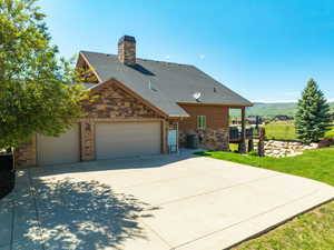 View of front of property with stone siding, a garage, a shingled roof, and a chimney