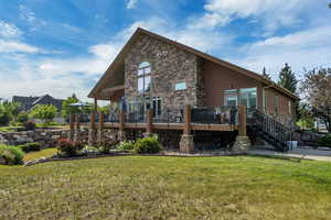 Back of property featuring stone siding, a yard, a wooden deck, and stairs
