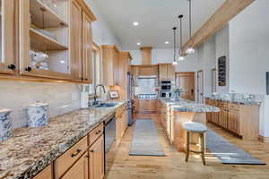 Kitchen featuring stainless steel appliances, light wood-type flooring, light stone counters, a breakfast bar, and recessed lighting