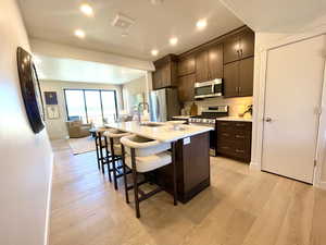 Kitchen featuring stainless steel appliances, a breakfast bar, dark brown cabinetry, light countertops, and light wood-style flooring