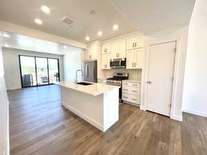 Kitchen with appliances with stainless steel finishes, wood finished floors, backsplash, an island with sink, and white cabinetry