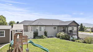 Rear view of house featuring a playground, roof with shingles, an outdoor structure, and a mountain view