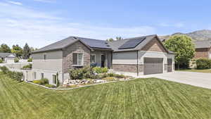 View of front of home with stone siding, an attached garage, driveway, and solar panels